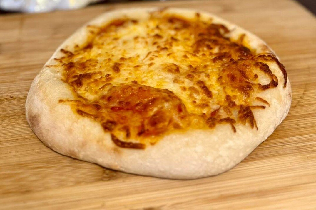 Pizza individual de masa madre con queso gratinado y borde dorado, sobre una tabla de madera