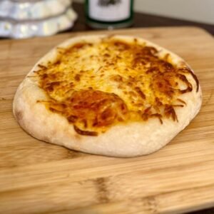 Pizza individual de masa madre con queso gratinado y borde dorado, sobre una tabla de madera