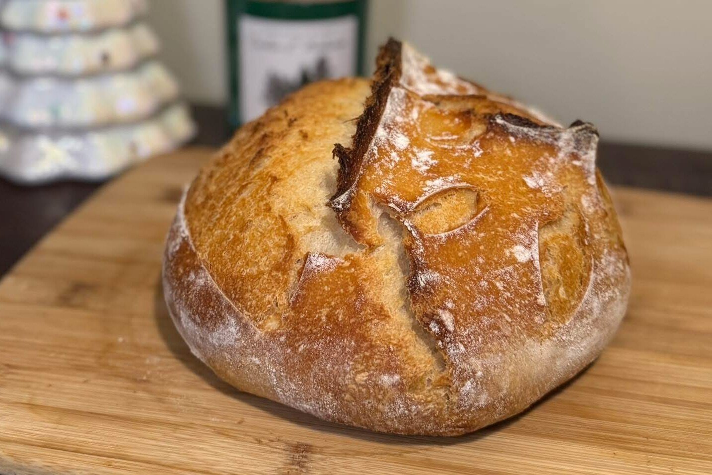 Pan de masa madre redondo con corteza dorada y un corte abierto, sobre una tabla de madera