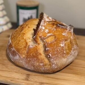 Pan de masa madre redondo con corteza dorada y un corte abierto, sobre una tabla de madera