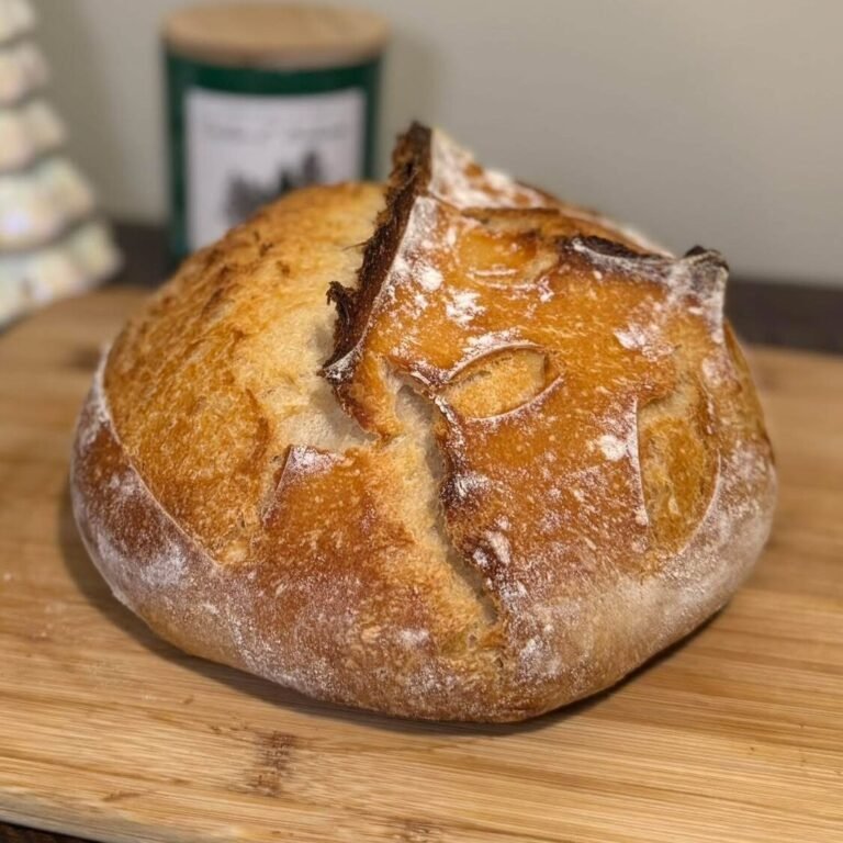 Pan de masa madre redondo con corteza dorada y un corte abierto, sobre una tabla de madera